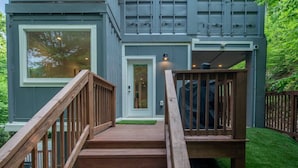 Une maison moderne avec un escalier en bois menant à la porte d’entrée, le tout entouré d’une pelouse bien entretenue.