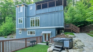 Une cabane à deux étages dotée d’une terrasse, entourée d’une clôture en bois et bordée d’un chemin en pierre.