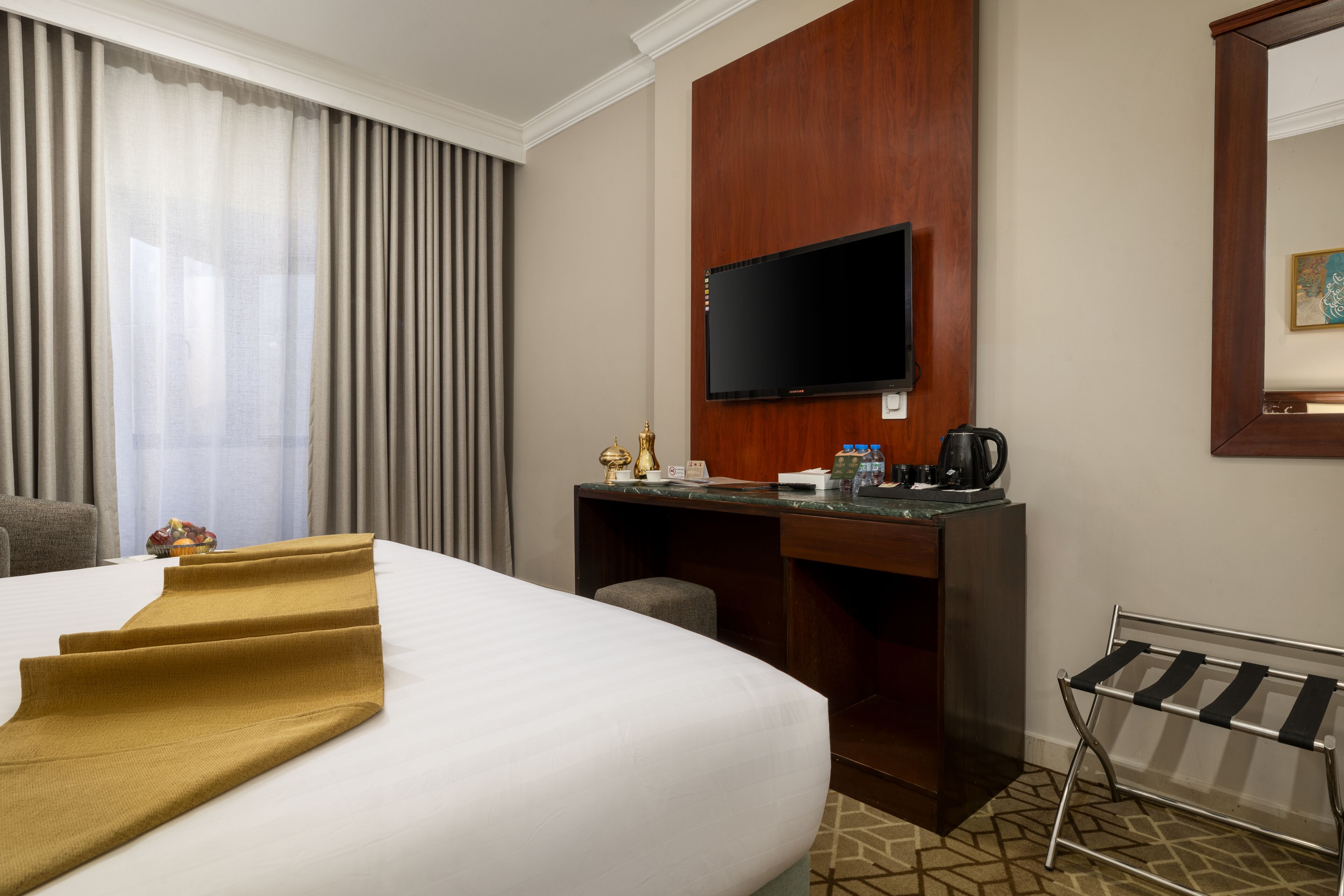 A hotel room with a large bed, a desk with a flat-screen TV, a coffee maker, and a bench.