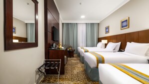A hotel room with two beds, a desk, a chair, a TV, and a mirror. - Emaar Al Manar (Makkah)