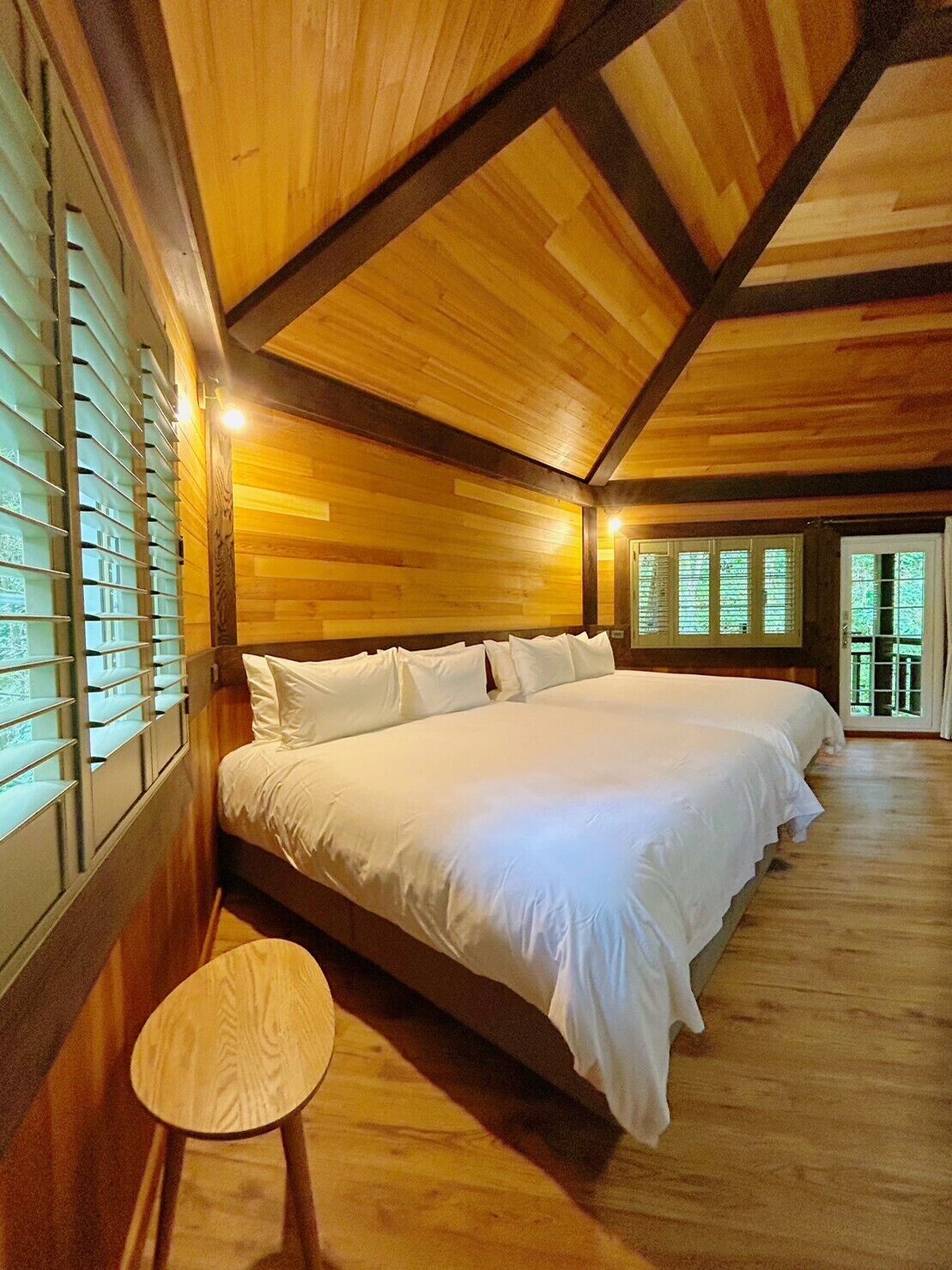 A large bed with white linens in a room with wooden walls and ceiling.