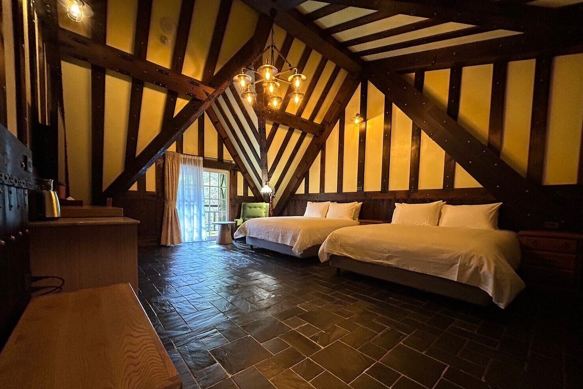 A room with two beds, a wooden ceiling, and a stone floor.