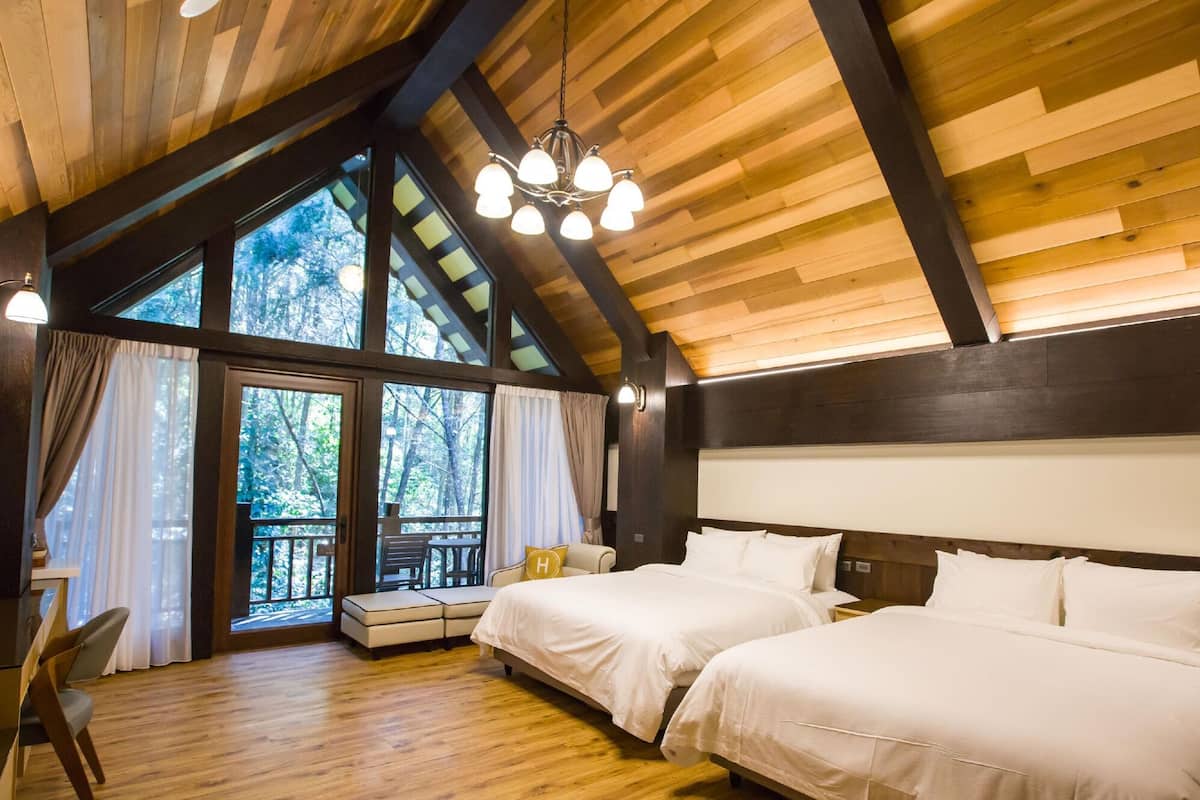 A bedroom with two beds, a wooden ceiling, and a large window with curtains.