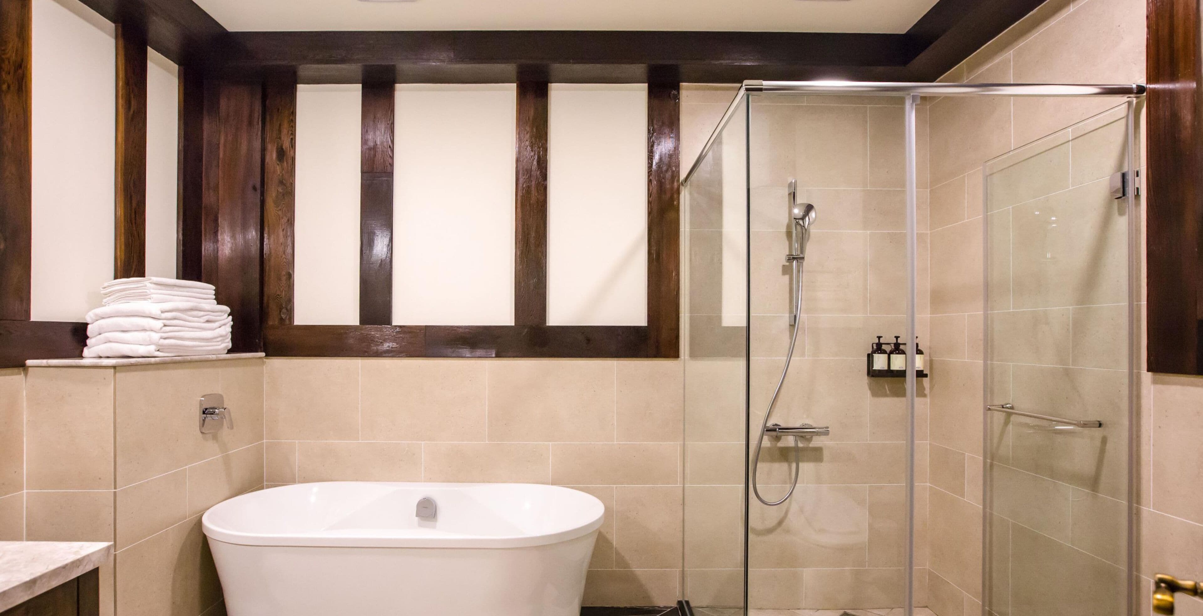 A bathroom with a freestanding bathtub, a glass-enclosed shower, and a stack of towels on a shelf.