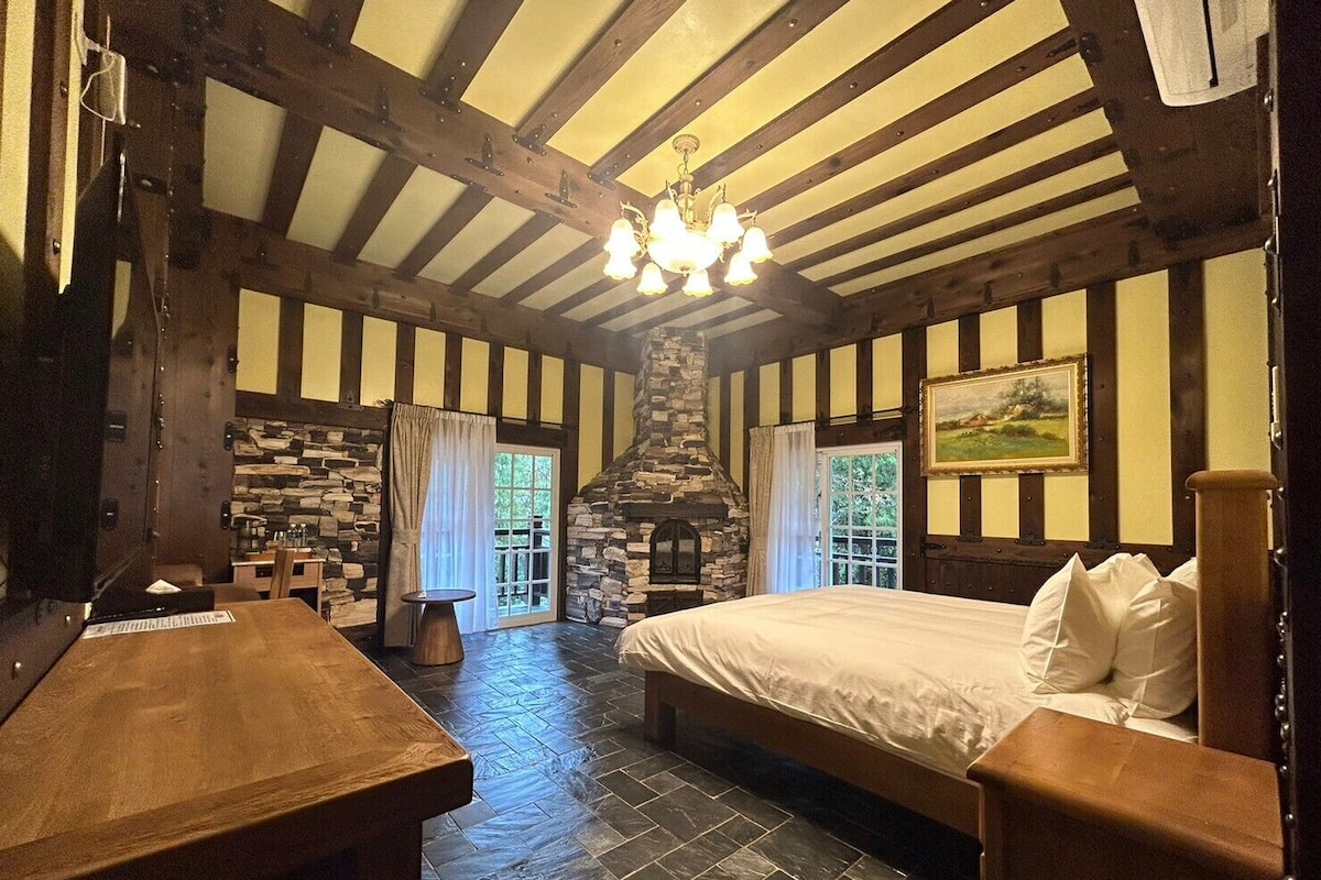 A room with a stone fireplace, wooden beams, a bed, and a table.