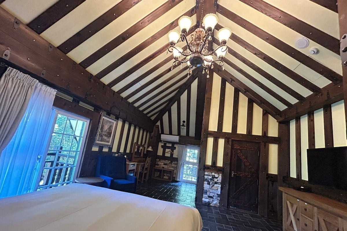 A room with a large bed, a chandelier, and a stone fireplace.