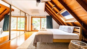 A bedroom with a large bed, a ceiling fan, a skylight, and a view of the outdoors. - Blissful Lakefront Pool & Oasis (Lake Munmorah)