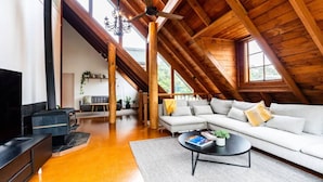 A spacious loft with a high ceiling, a fireplace, a sofa, and a television. - Blissful Lakefront Pool & Oasis (Lake Munmorah)