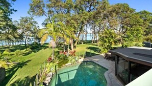 A pool surrounded by tropical vegetation and a modern building structure. - Blissful Lakefront Pool & Oasis (Lake Munmorah)