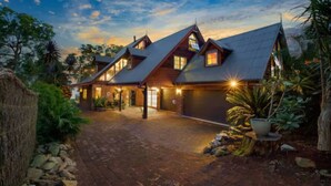 A large, multi-story building with a steeply pitched roof, multiple chimneys, and a well-lit entrance. - Blissful Lakefront Pool & Oasis (Lake Munmorah)