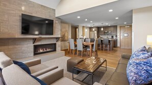 Una sala de estar moderna con chimenea, un televisor de pantalla plana y una zona de comedor con cocina al fondo.
