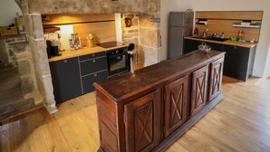 Une cuisine avec un mur en pierre, des armoires en bois, un four encastré et un îlot central en bois.