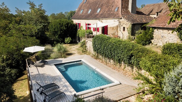 Une maison avec une piscine, entourée de verdure et d’un mur de pierre.