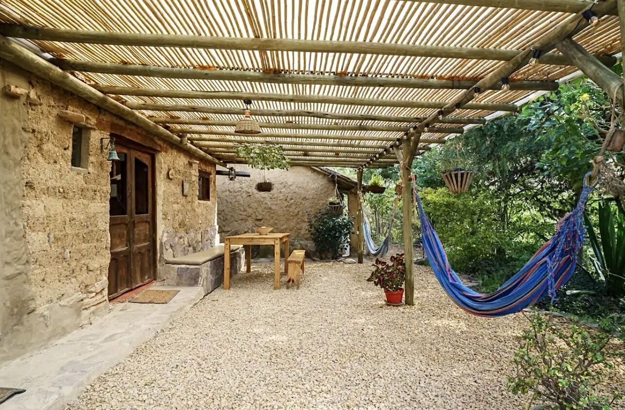 An outdoor patio with a bamboo roof, a wooden table, and a hammock.
