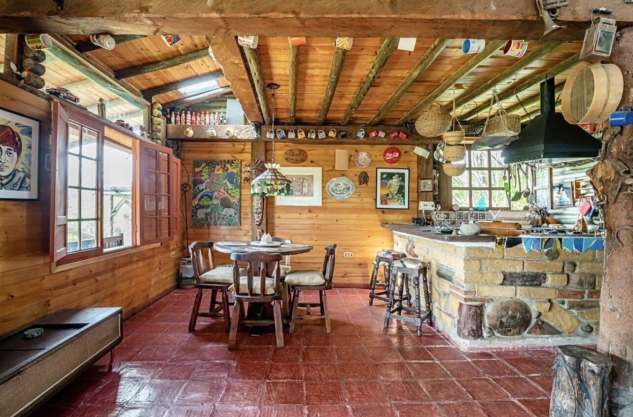 A rustic wooden interior with a wooden ceiling, a round table with chairs, and a stone counter with various items.