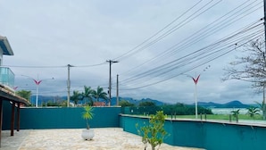 A rooftop terrace with stone flooring, potted plants, and a view of the sea and mountains. - Pousada Riviera  (Caraguatatuba)