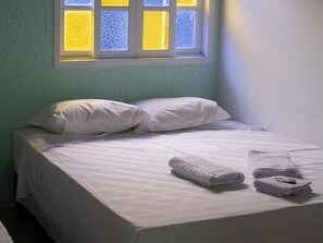 A small, neatly made bed with white linens and pillows, a window with a view of a yellow building, and a folded towel on the bed. - Pousada Riviera  (Caraguatatuba)