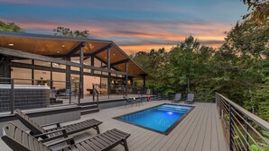 Un espace piscine extérieur moderne, doté d’une terrasse en bois, de chaises longues et d’un coin salon abrité.