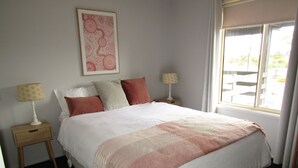A neatly made bed with a white and pink blanket, two bedside tables with lamps, and a window with a view of the outdoors. - Hooked on Hardwicke - Short walk to the beach!  Off Peak special! (Hardwicke Bay)