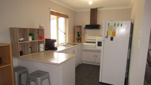 A compact kitchen with a sink, stove, and refrigerator. There are bar stools and a window with blinds. - Hooked on Hardwicke - Short walk to the beach!  Off Peak special! (Hardwicke Bay)