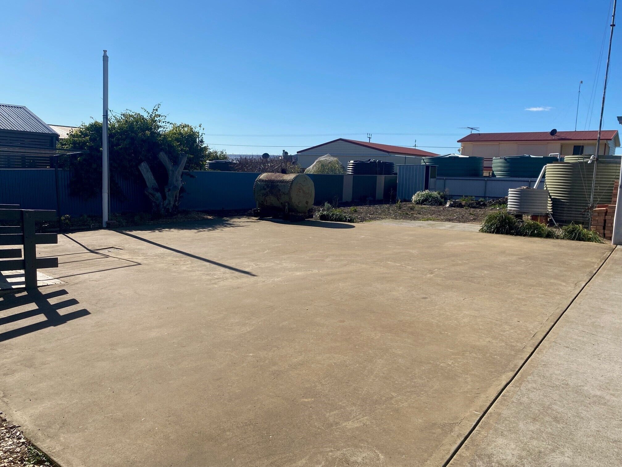 A concrete parking area with a metal fence, a large cylindrical object, and a building with a red roof in the background.