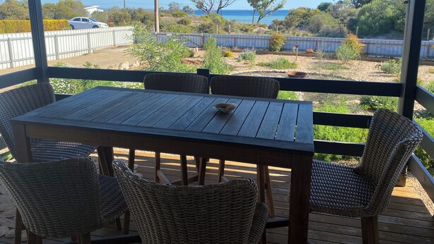 A covered outdoor seating area with a table and wicker chairs, overlooking a landscaped garden and a view of the sea. - Hooked on Hardwicke - Short walk to the beach!  Off Peak special! (Hardwicke Bay)