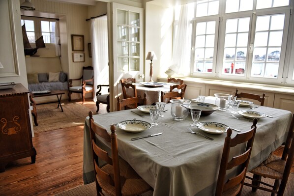 A dining room with a table set for four, wooden chairs, and a window with a view. - House "henri Chardon" , A travel on the sea ! (Barfleur)