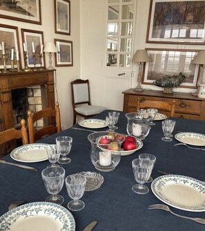 A dining room with a table set for four, featuring floral-patterned plates, clear glassware, and a fruit bowl. - House "henri Chardon" , A travel on the sea ! (Barfleur)