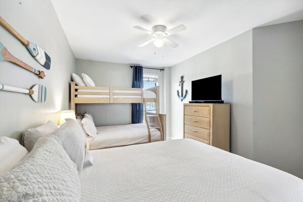 A bedroom with bunk beds, a ceiling fan, a TV, and a dresser. - Pelican Pointe 804 by Liquid Life (Orange Beach)