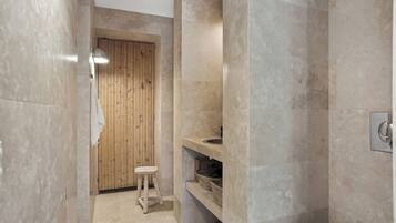Un baño moderno con puerta de madera, un taburete pequeño, un lavamanos y una repisa con cestas.