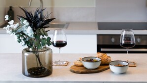 A modern kitchen with white cabinets, a glass vase with flowers, two glasses of red wine, and a wooden board with bread and olives. - Urban Oasis by Keystone (Newport)