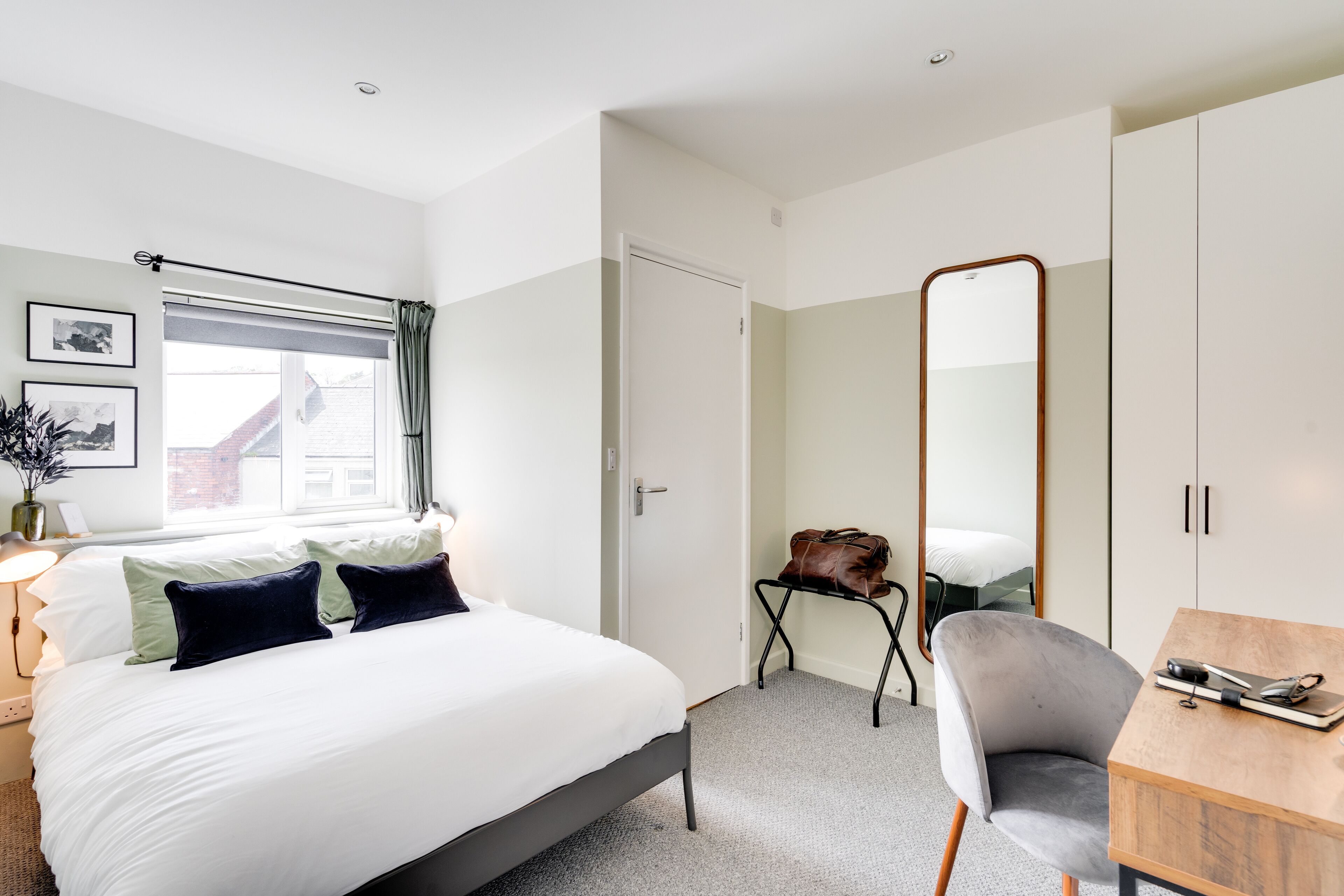 A modern bedroom with a bed, a desk, a chair, a large mirror, and a wardrobe.