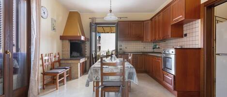 A kitchen with wooden cabinets, a dining table with chairs, a built-in oven, and a hanging light fixture.