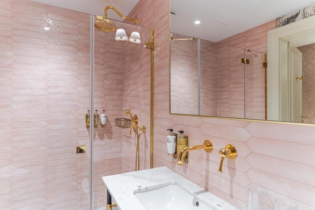 Un baño moderno con cabina de ducha de vidrio, lavamanos blanco y detalles dorados.