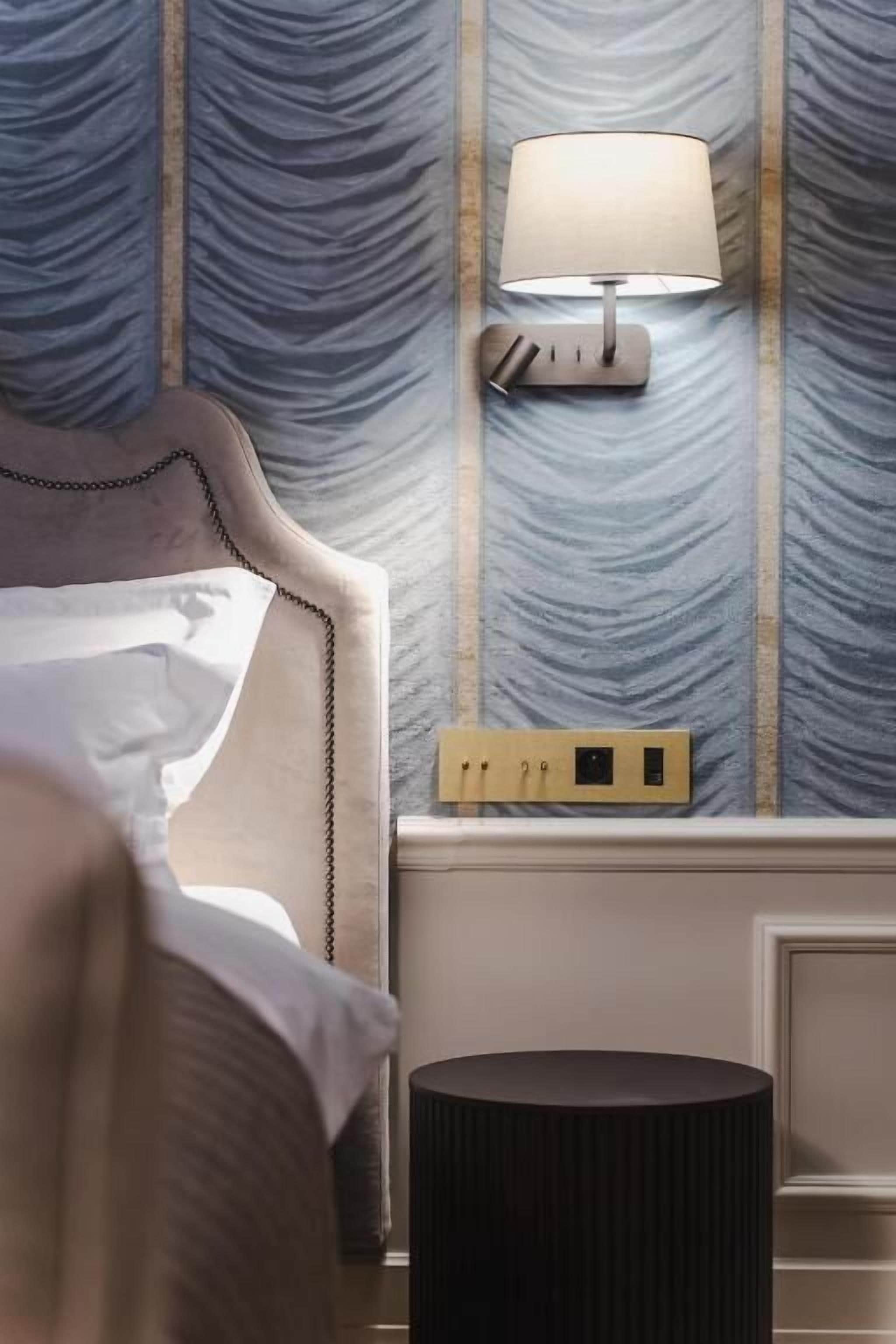 Habitación de hotel con cama, lámpara de noche, mesita de noche y pared con textura.