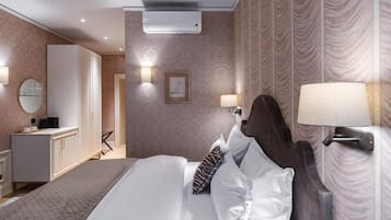 A hotel room with a bed, bedside lamps, a wardrobe, and an air conditioning unit.