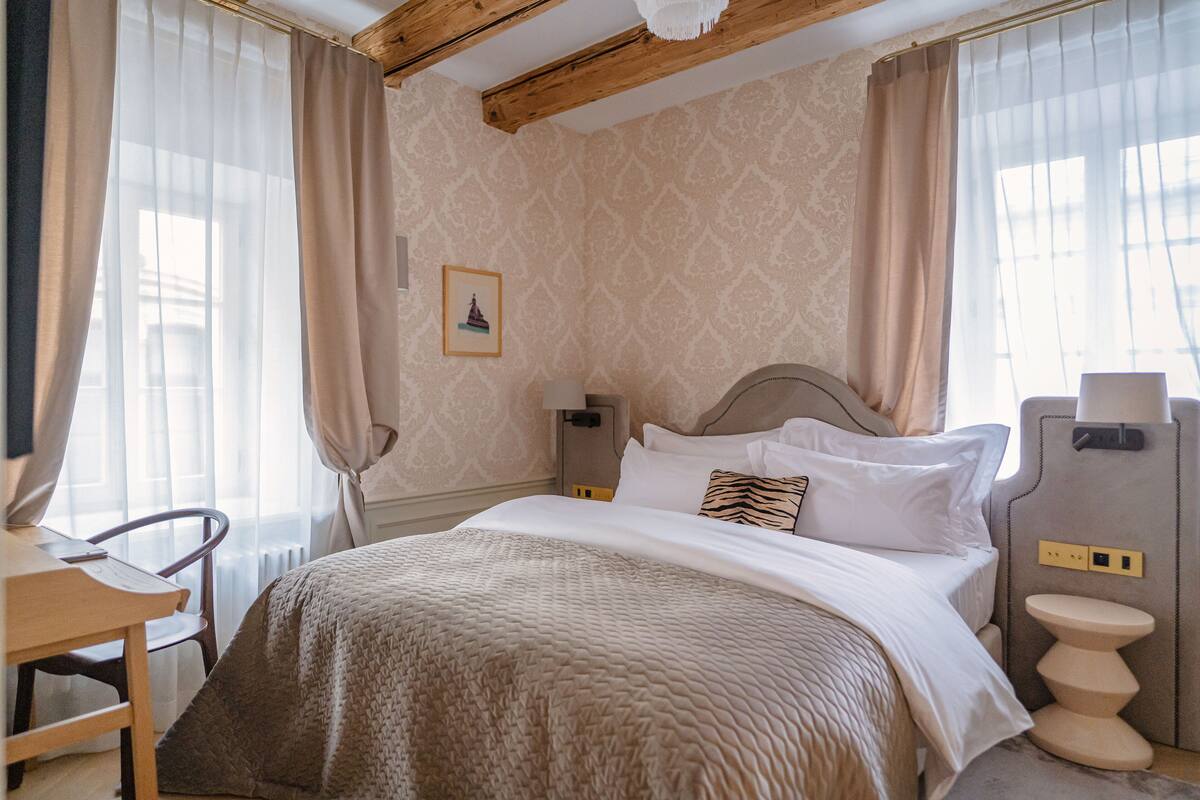 A hotel room with a bed, a chair, a nightstand, and a wall-mounted toilet.