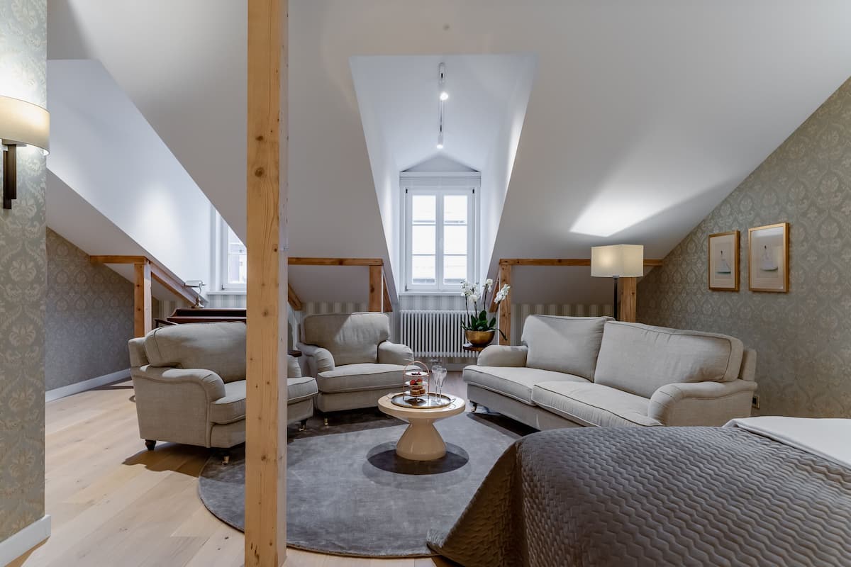 A spacious loft bedroom with a high ceiling, a large window, and a cozy seating area with a sofa and armchairs.