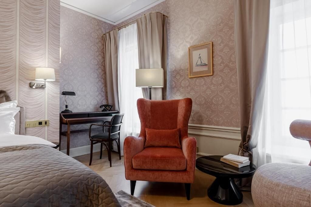 A hotel room with a bed, a desk, a chair, and a small table with books.