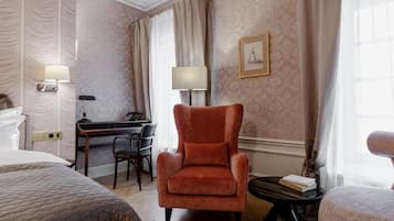 A hotel room with a bed, a desk, a chair, and a small table with books.