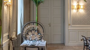 Comedor con una mesa preparada para dos personas, sillas, una planta en maceta e iluminación instalada en la pared.