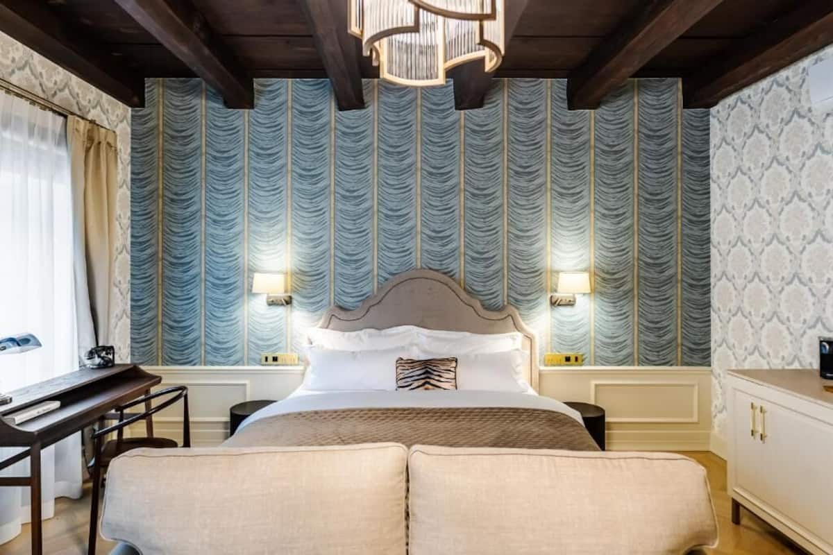 A hotel room with a large bed, a desk, and a chair. There are two wall-mounted lamps on either side of the bed.