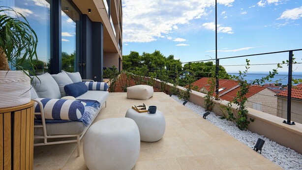 A modern outdoor seating area with a sofa, ottomans, and a table, overlooking a scenic view of the sea and buildings. - Hedera Estate, Hedera Studio 1 (Dubrovnik)
