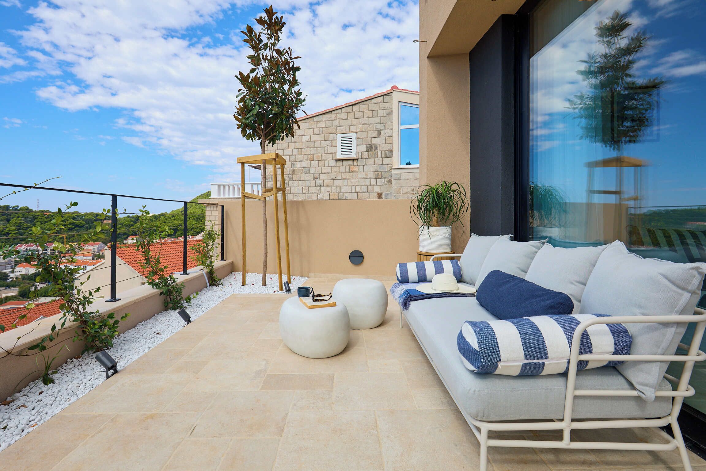 A balcony with a white sofa, round ottomans, and a potted plant.