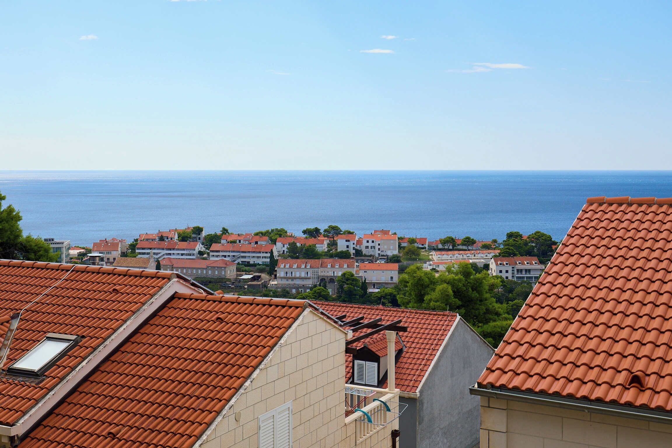 A coastal residential area with terracotta-tiled rooftops and a clear view of the sea.