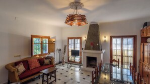 A living room with a sofa, a glass coffee table, a fireplace, and a dining table with chairs. - Casa Rural Andaluza, Rodeada de Vegetación, Piscina. Ideal Vacaciones en Familia (Alhaurín de la Torre)