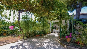 A narrow pathway lined with potted plants and trees, leading to a seating area with a table and chairs. - Casa Rural Andaluza, Rodeada de Vegetación, Piscina. Ideal Vacaciones en Familia (Alhaurín de la Torre)