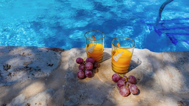 Two glasses of orange juice and a bunch of grapes on a stone surface by a pool. - Casa Rural Andaluza, Rodeada de Vegetación, Piscina. Ideal Vacaciones en Familia (Alhaurín de la Torre)