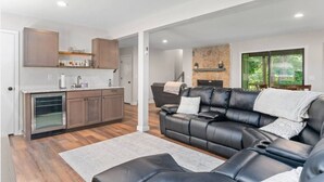 A modern kitchen with wooden cabinets and a built-in oven, a leather sofa with cushions, and a stone fireplace.