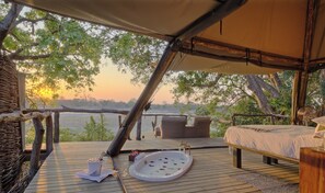 A tented accommodation with a bed, a small table with a fan, and a hot tub. - Shawa Luangwa Camp (South Luangwa National Park)